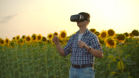 A-young-man-in-plaid-shirt-and-jeans-uses-VR-glasses-on-the-field-with-sunflowers-in-sunny-day.-These-are-modern-technologies-in-summer-evening.